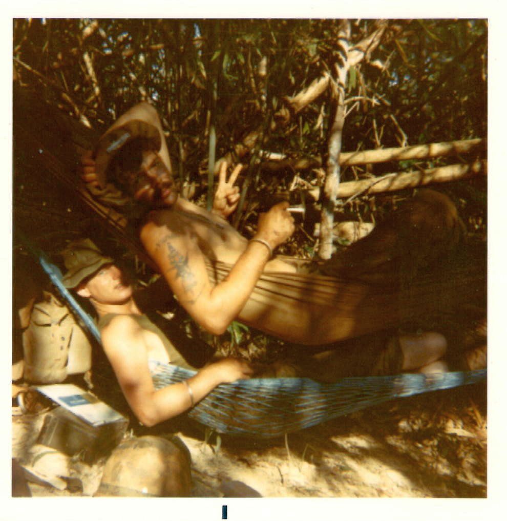 Jeff (in blue hammock) with squad leader and friend Gary Kelch (smoking a joint and giving V sign). Most grunts wore Montangard bracelets like the one Gary wears on his wrist. Jeff''s was lost after he was wounded. Gary visited Jeff at 24th Evac. He removed his bracelet and gave it to Jeff. Song Be, Vietnam 1970