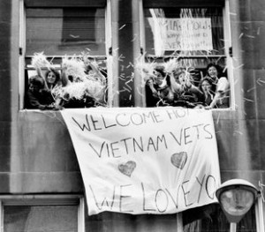 Tens of thousands of Vietnam War veterans today formed the biggest parade in the city's history, marching across the Brooklyn Bridge and down Broadway in a lavish ticker-tape "welcome home" that was 10 years late. Tons of ticker tape and confetti, obliterating street signs in a blizzard of white, showered down on the 25,000 veterans as they wound through the financial district at the lower tip of Manhattan. Brooklyn, 1985