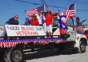 Veterans Day parade tow truck with sign, flag, civilians.